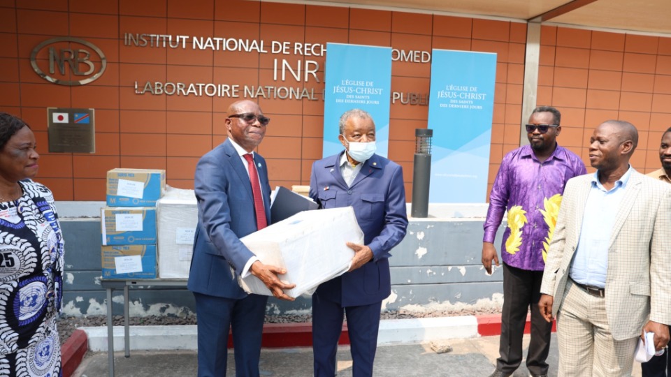 Elder Mwanke Baker David Ngabizele, Soixante-dix d’Interrégion, présente un échantillon d’équipements remis en don à Dr. Jean-Jacques Muyembe, Directeur Général de l’INRB, à Kinshasa, RDC, en présence de membres du staff, le 16 juillet 2026.